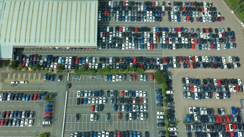 Home Aerial shot of a vast parking lot filled with parked vehicles and a large building.